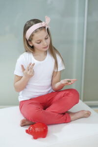 Girl with red piggy bank counting coins on bed